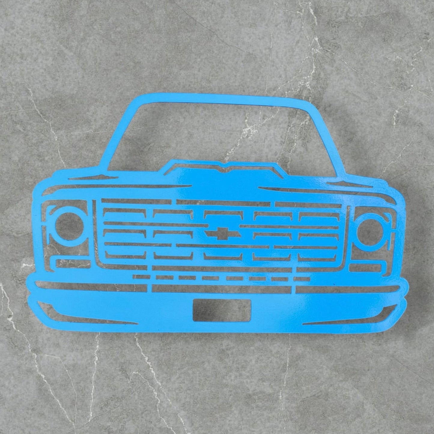 Blue metal cutout of a car's front grille on a gray marble background