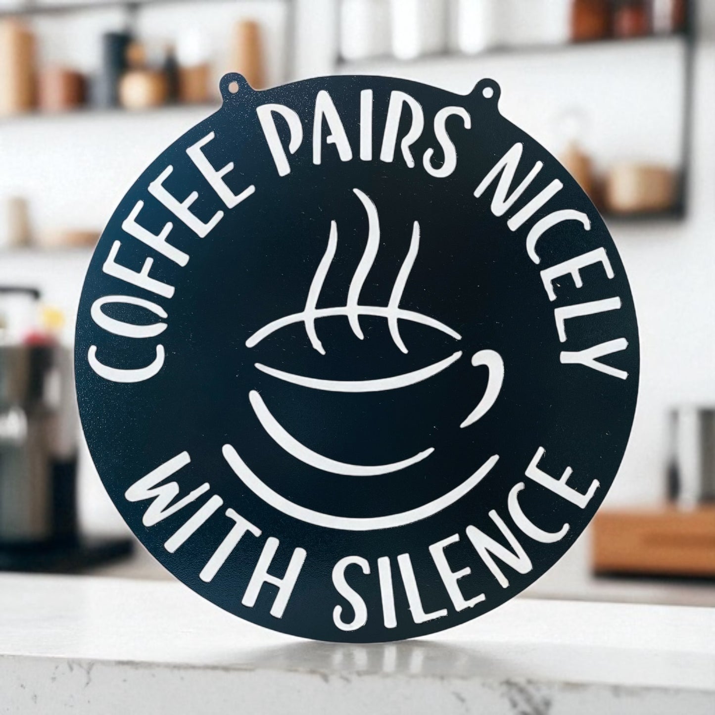 Decorative sign with coffee cup and text 'Coffee pairs nicely with silence' on a kitchen counter.