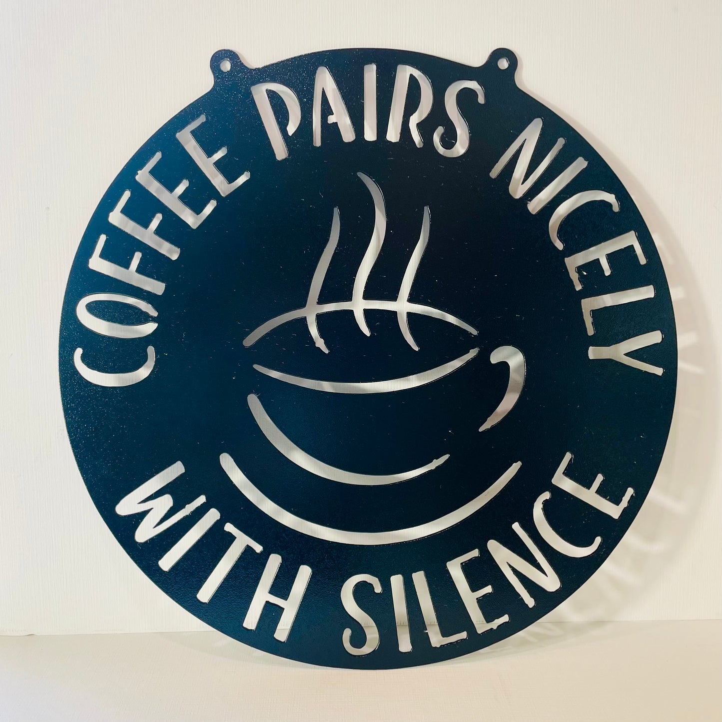Decorative metal sign with coffee cup design and text 'Coffee pairs nicely with silence' on a white background.