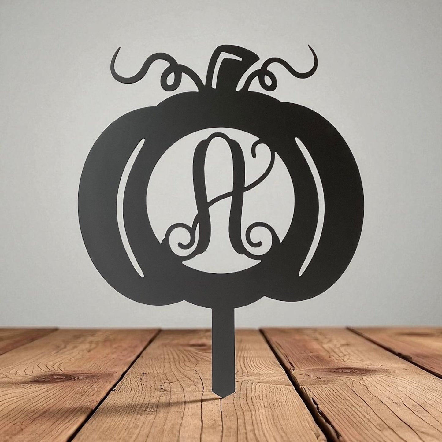 Black pumpkin-shaped monogram with 'A' on a wooden stand against a gray background