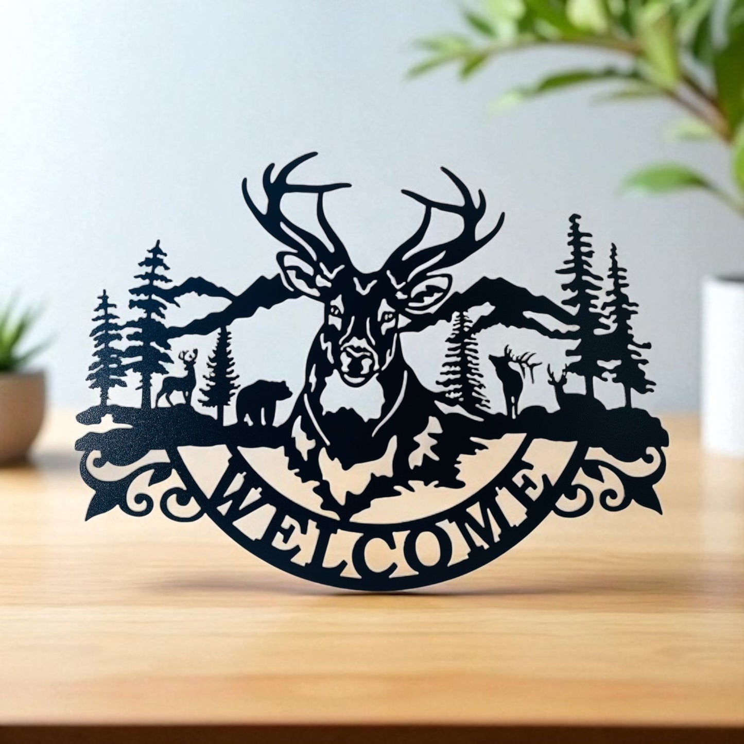 Decorative metal sign with a deer design and 'Welcome' text on a wooden surface.