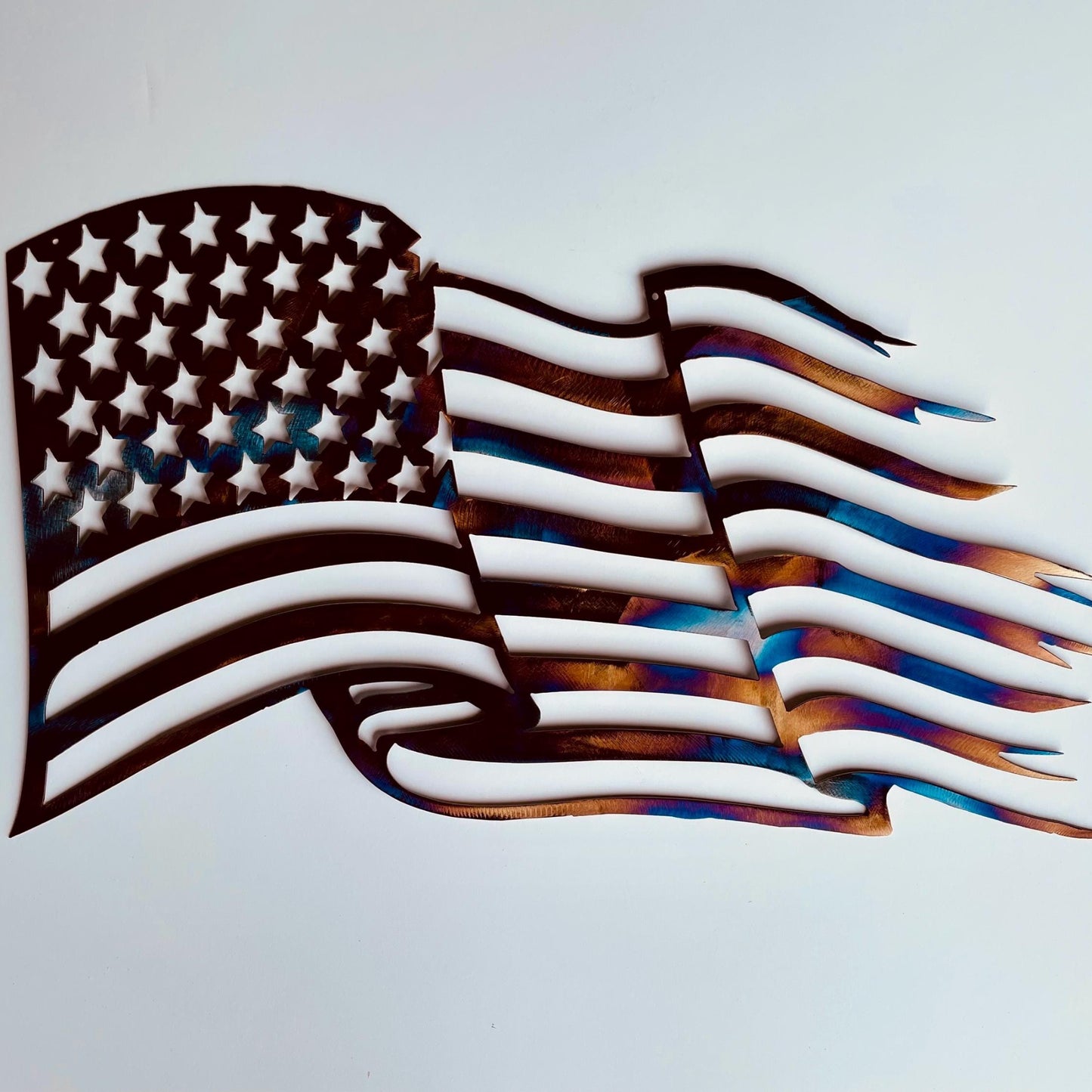 Multicolored metal American flag which looks like it is tattered and waving in the wind.