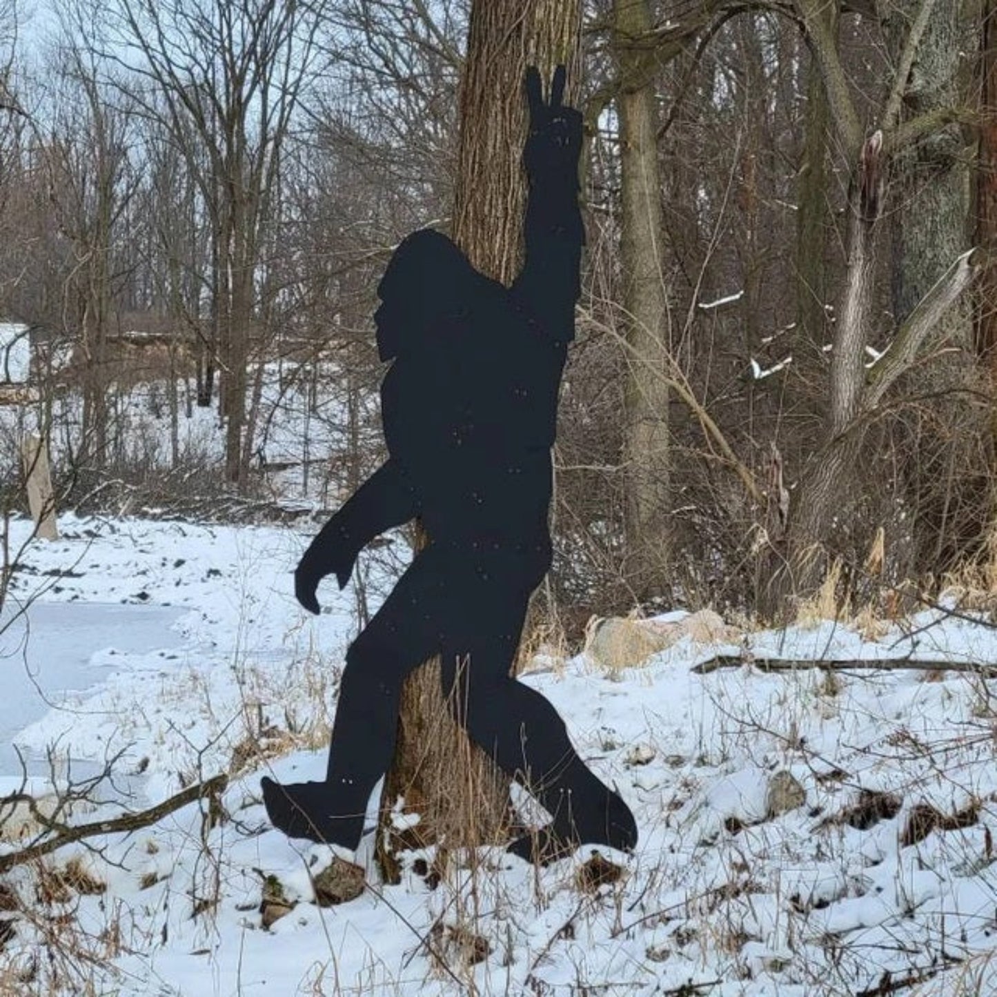 Black silhouette of a metal Bigfoot against a snowy forest background