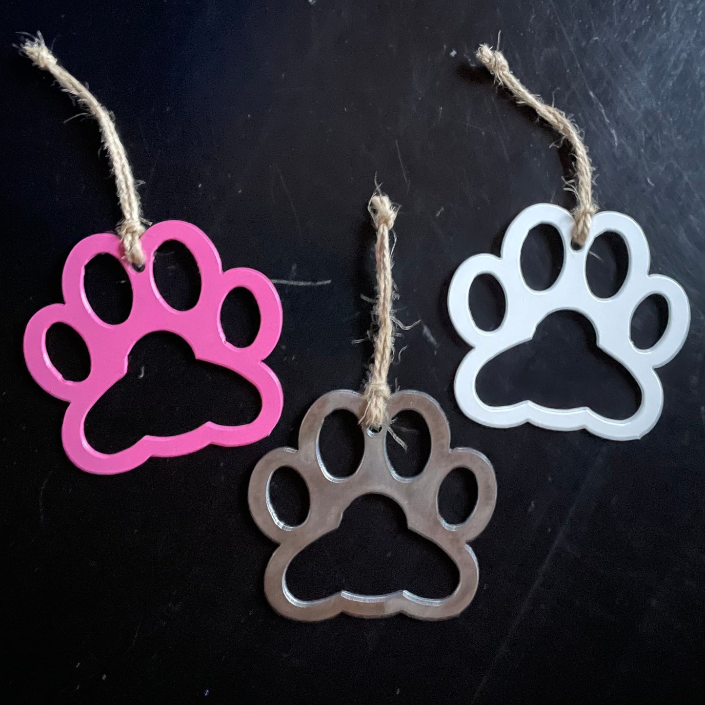 Three paw-shaped keychains in pink, silver, and white on a black background.