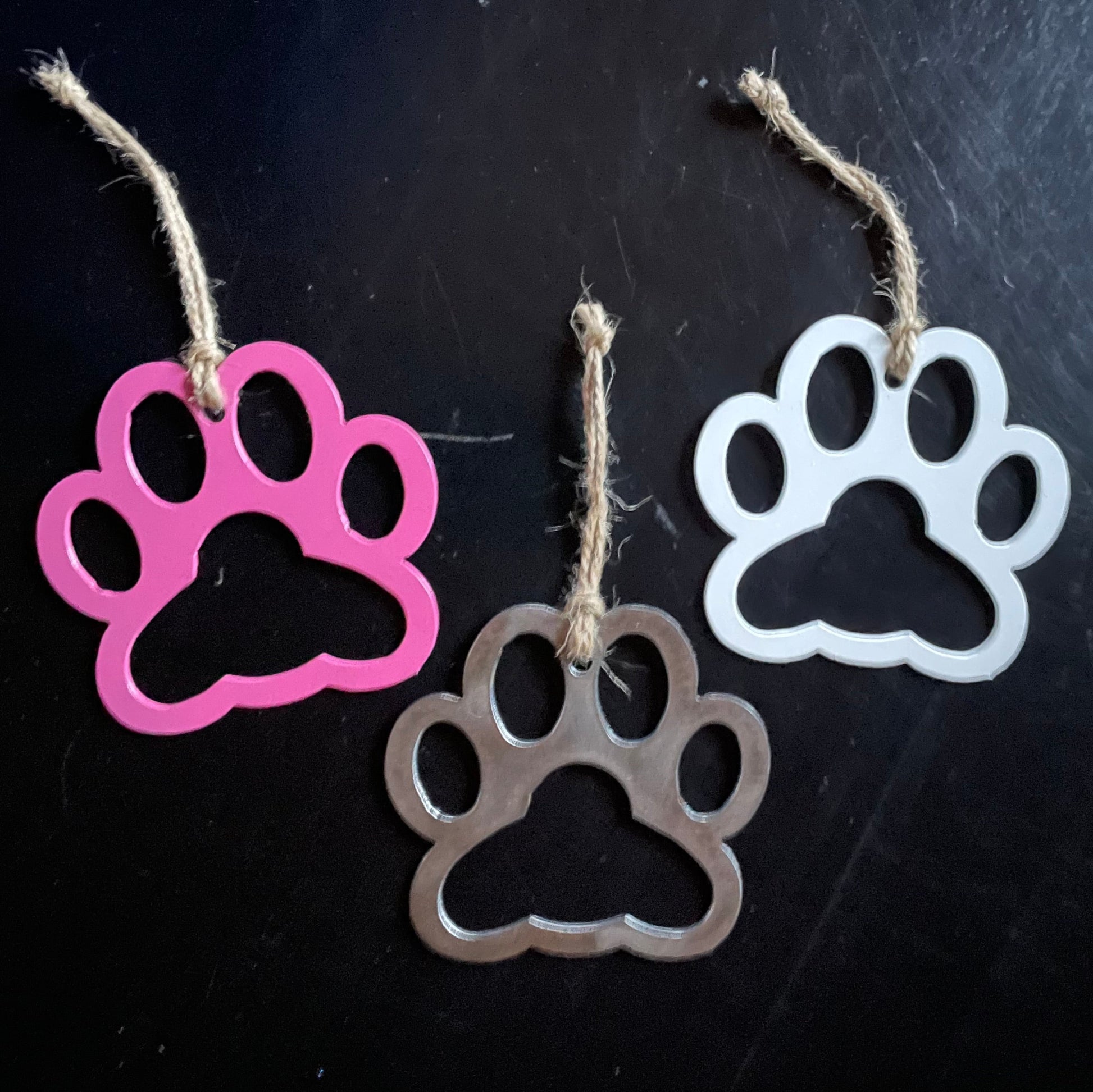 Three paw-shaped keychains in pink, silver, and white on a black background.
