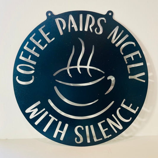 Decorative metal sign with coffee cup design and text 'Coffee pairs nicely with silence' on a white background.