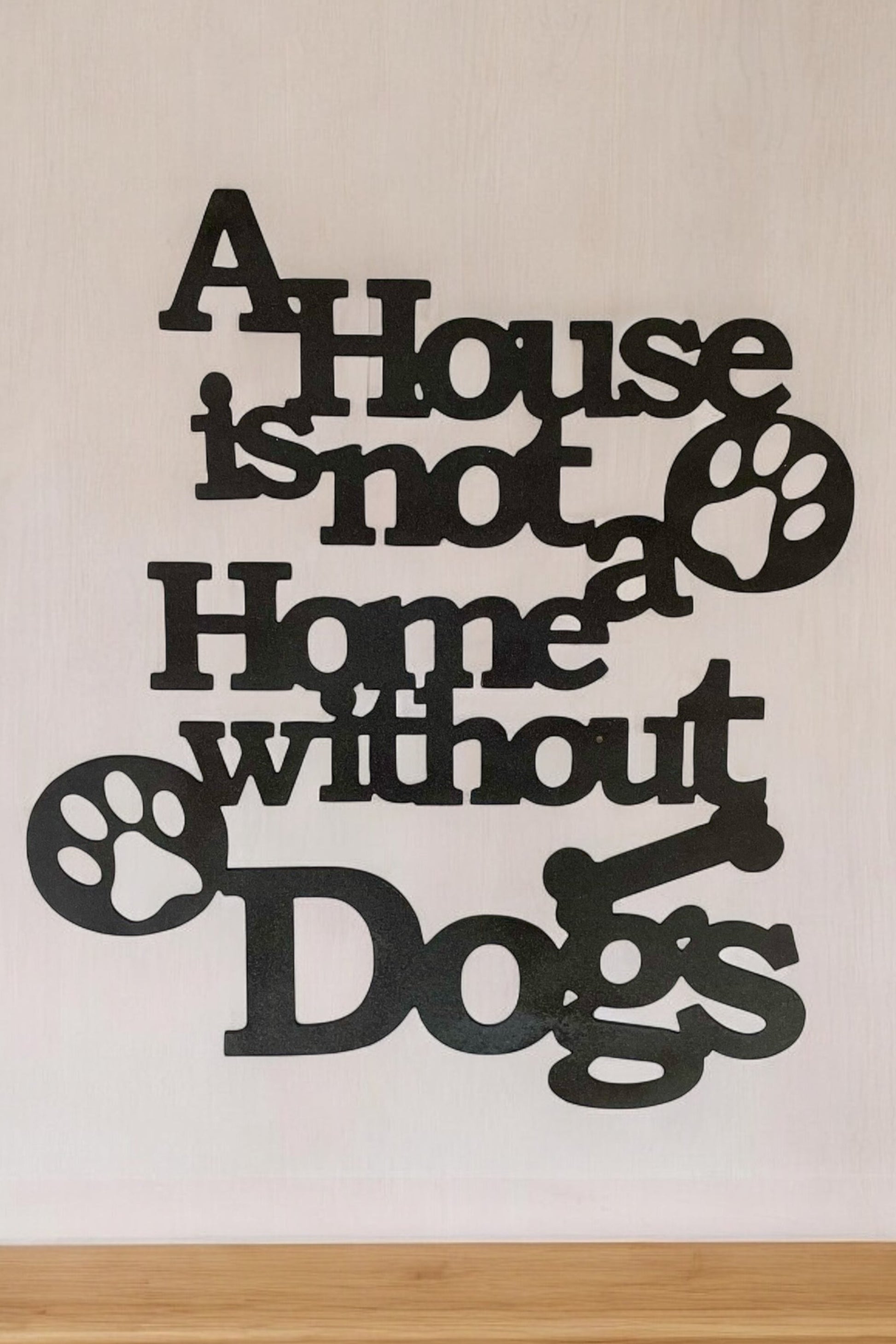 Metal wall sign that reads" A house is not a home without dogs" in black