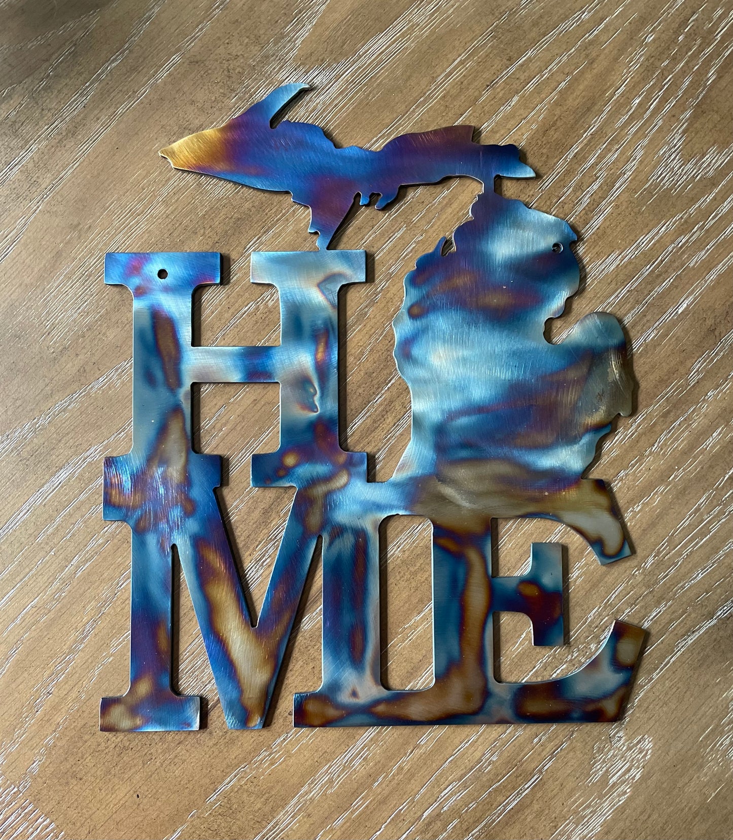 Decorative metal sign with 'HOME' and Michigan design on a wooden surface