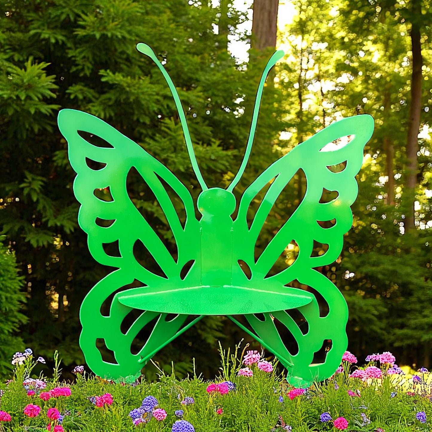Green butterfly-shaped garden stake in a garden setting with flowers and trees.