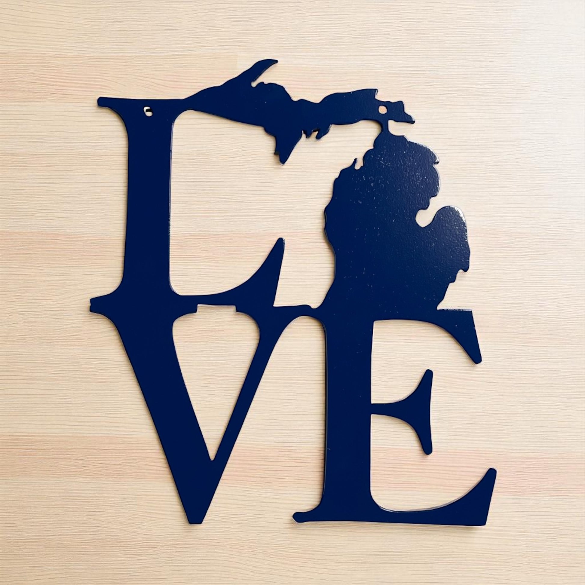 Blue metal cutout of the state of Michigan shaped like the word 'LOVE' on a wooden surface.