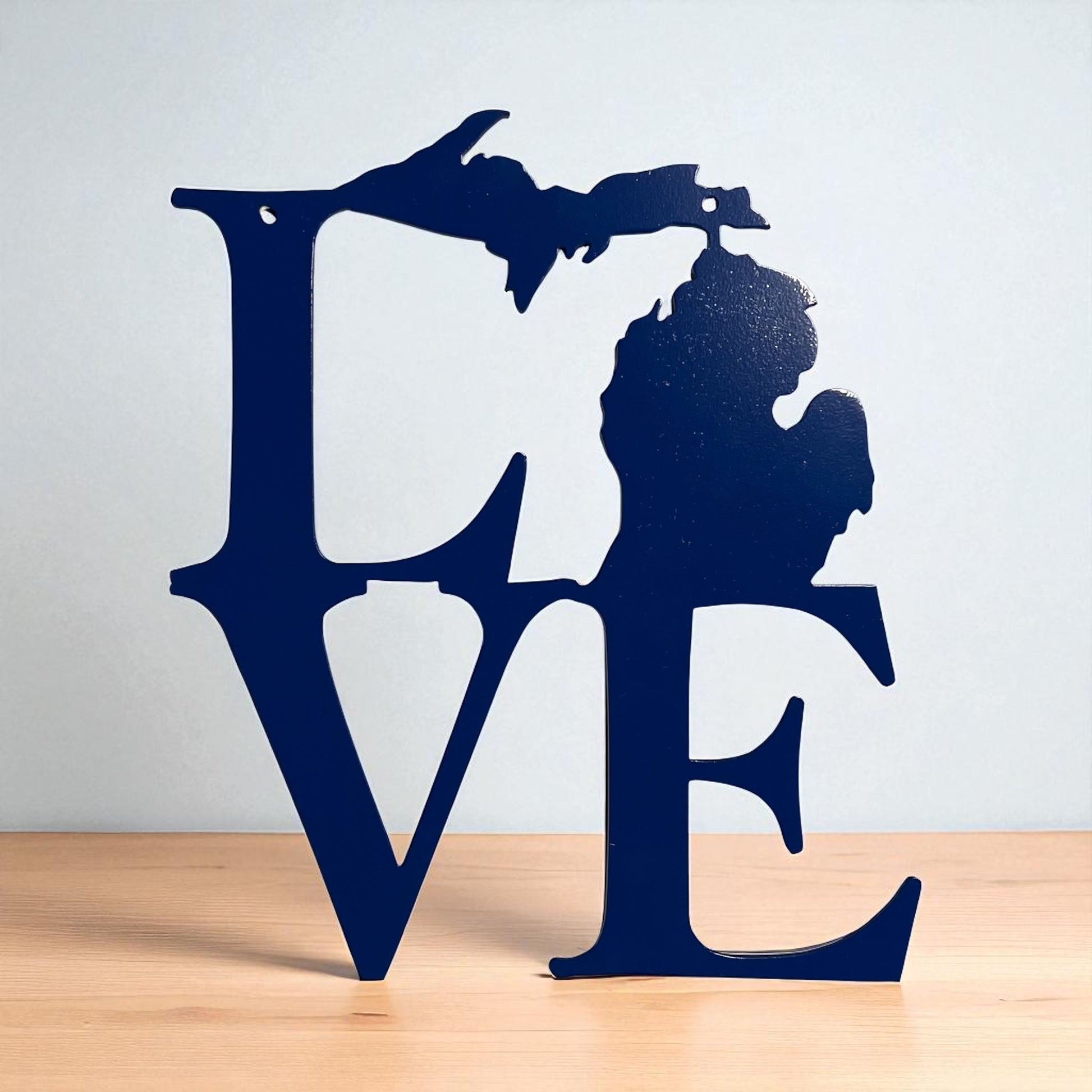 Navy blue metal decorative sign with 'LOVE' and Michigan silhouette on a wooden surface and light gray background