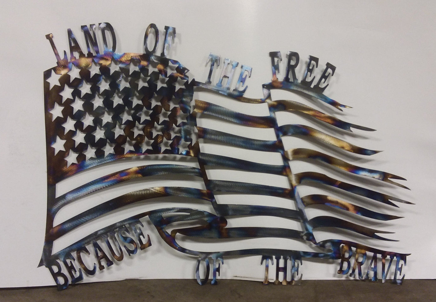 Metal American flag made to look like it is blowing in the wind with the words " Land of the free because of the brave"
