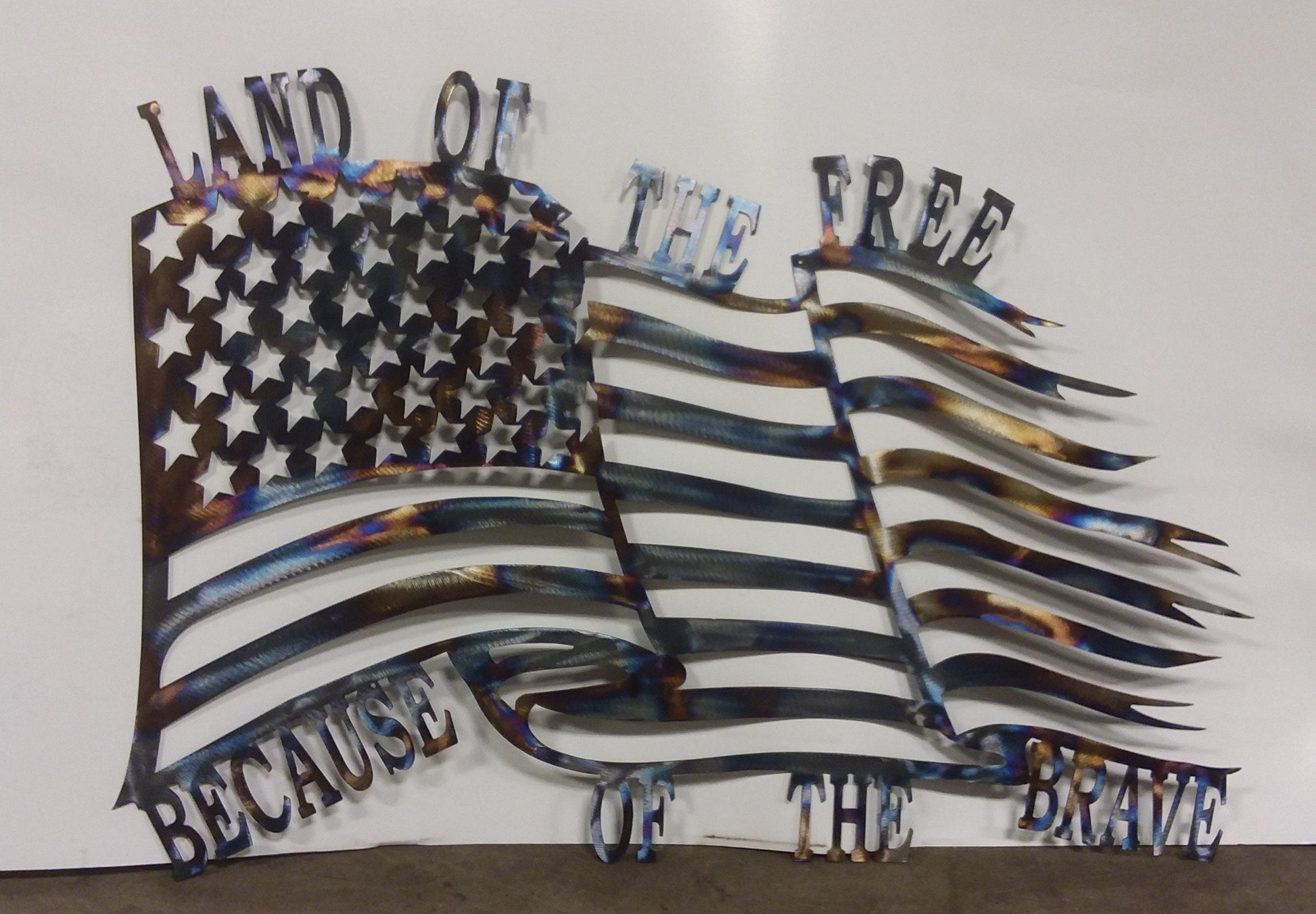 Metal American flag made to look like it is blowing in the wind with the words " Land of the free because of the brave"